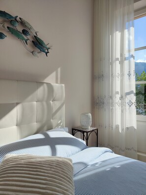 Une chambre à coucher avec un lit, une table de chevet, une décoration murale représentant des poissons et une fenêtre avec des rideaux.