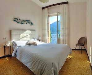 A bedroom with a bed, a chair, a nightstand, a decorative fish wall art, and a view of the outdoors.
