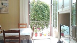 Un comedor con mesa y sillas, vistas a un balcón con plantas en macetas y un televisor montado en la pared.