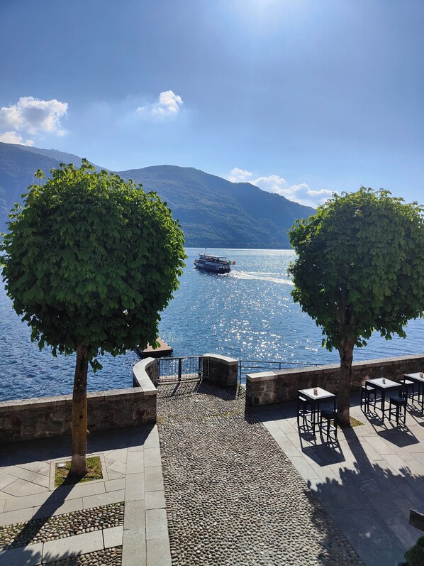 A waterfront terrace with stone flooring, two trees, and a boat on the water.
