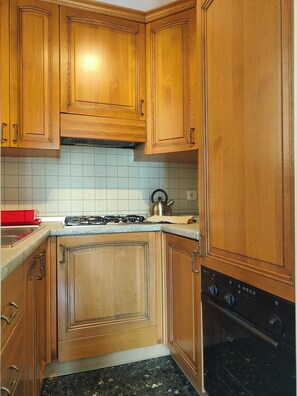 A kitchen with wooden cabinets, a gas stove, a kettle, and a built-in oven.