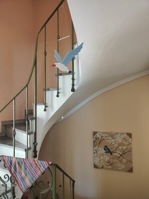 Un escalier avec une rampe en métal, une décoration représentant un oiseau suspendue et un tableau représentant un oiseau accroché au mur.