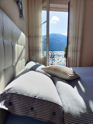 A bedroom with a large bed, a headboard, and a view of the outdoors through a window.