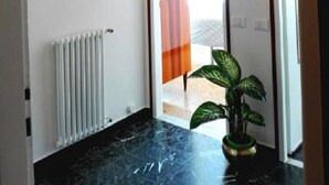 Un pasillo con un radiador, un espejo, una lámpara colgante y una planta en maceta.