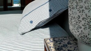 Una cama con ropa de cama a rayas, una almohada estampada y un jarrón decorativo.