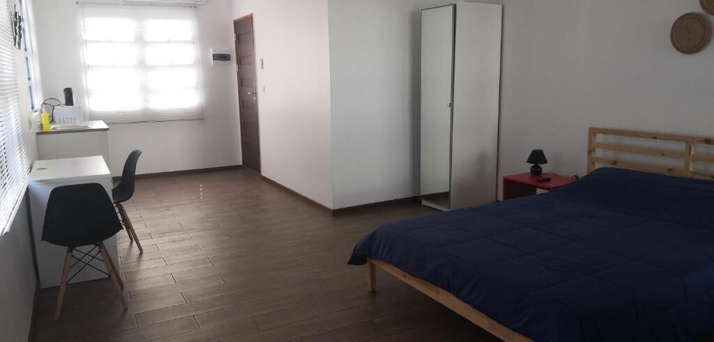A bedroom with a bed, a desk with a chair, a wardrobe, and a window.