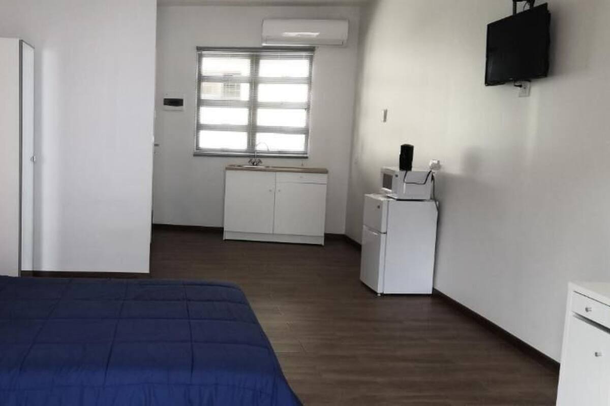A bedroom with a bed, a wardrobe, a desk, a window, and a TV.