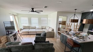 En rummelig stue med sofa, fjernsyn og spiseområde med køkkenø.