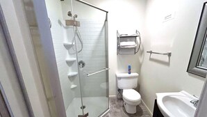 Et badeværelse med brusekabine i glas, toilet, vask og spejl.