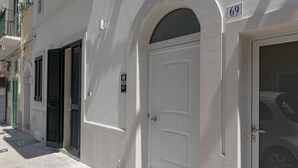 A white building with a large arched doorway and a door with a number 69 sign above it. - Historic citycentre apartment with breathtaking views (Monopoli)