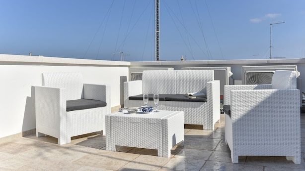 A rooftop terrace with white wicker furniture, including a sofa and two armchairs, a small table with a bowl and glasses, and a view of the sky and power lines. - Historic citycentre apartment with breathtaking views (Monopoli)