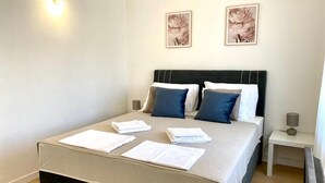 A neatly made bed with pillows and folded towels, a bedside table with a lamp, and two framed pictures on the wall. - Villa Mihaela - Beachfront apartment "Mario" with sea view and pool (Cesarica)