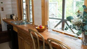 A kitchen with a wooden countertop, a sink, a bowl of fruit, and a pitcher.