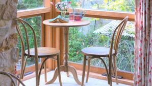 A corner room with a wooden table and two chairs, a window with curtains, and a hanging light fixture.