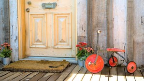 A wooden door with a brass handle, a doormat, potted plants, and a red wheelbarrow.