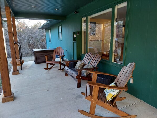 A porch with wooden rocking chairs and a bench, a small table, and a wooden cabinet.