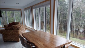 A modern dining area with a wooden table and chairs, large windows with a forest view, and a patterned sofa. - Lake Front spacious family home (Eagle Rock)