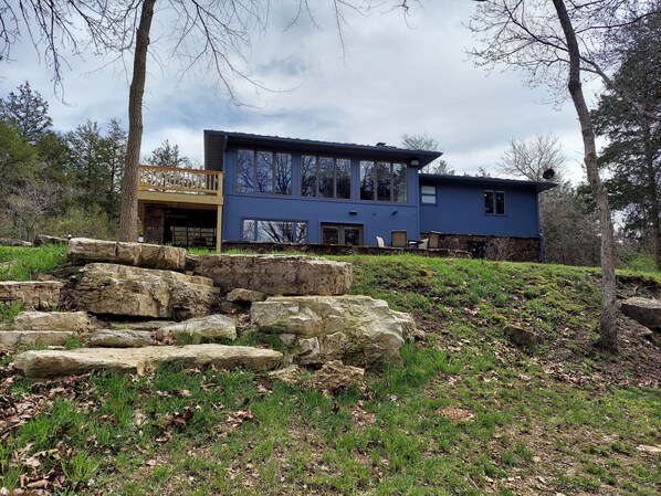 A modern two-story house with a stone foundation, large windows, and a balcony.
