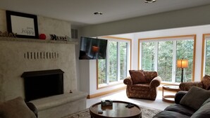 A living room with a fireplace, a television, and large windows with a view of trees. - Lake Front spacious family home (Eagle Rock)