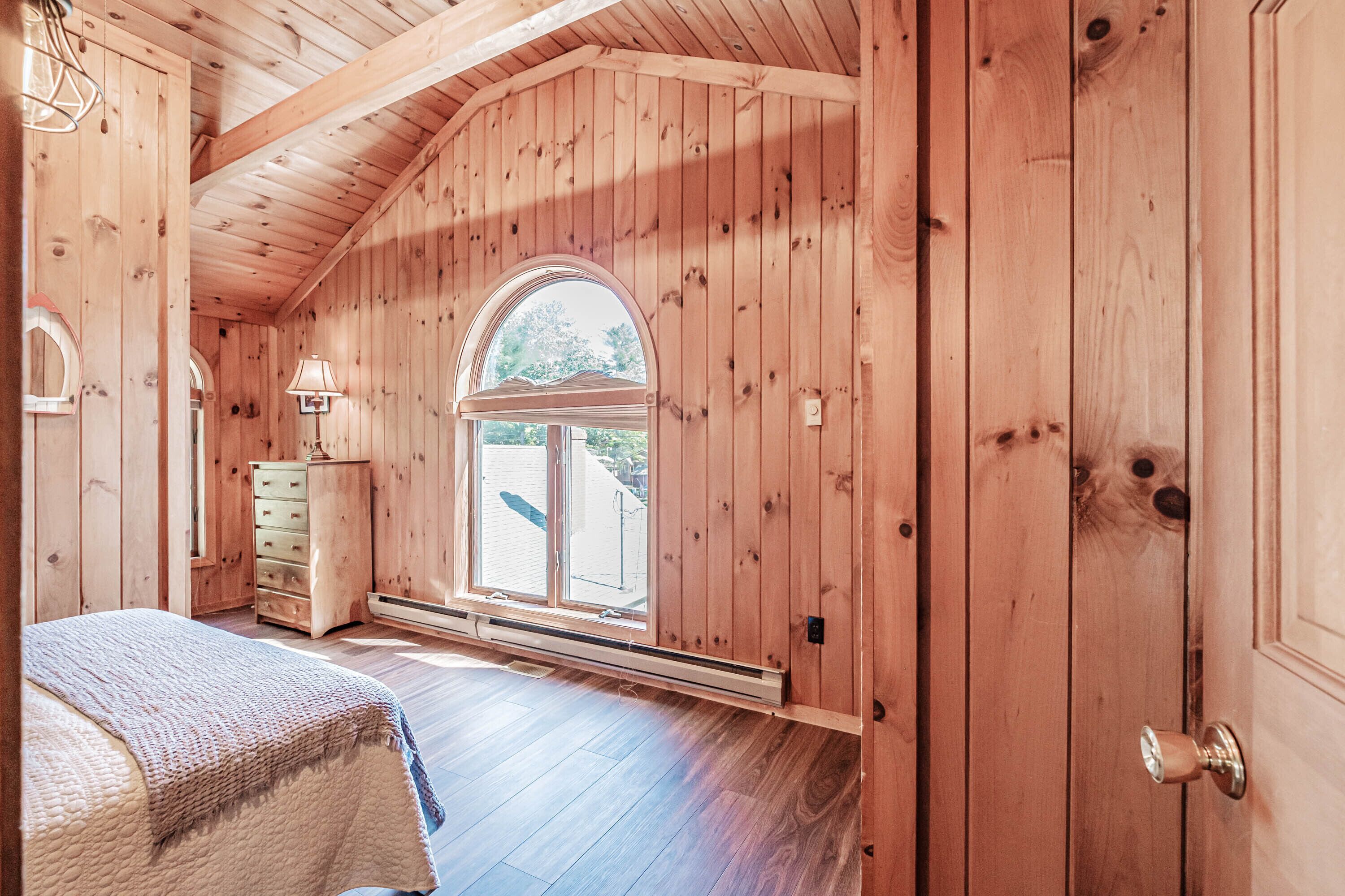 A wooden room with a bed, a dresser, a window, and a door.