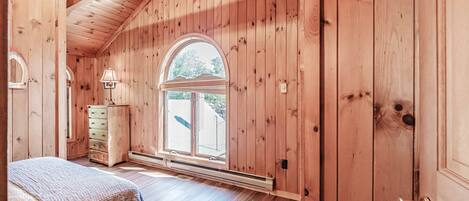 A wooden room with a bed, a dresser, a window, and a door.