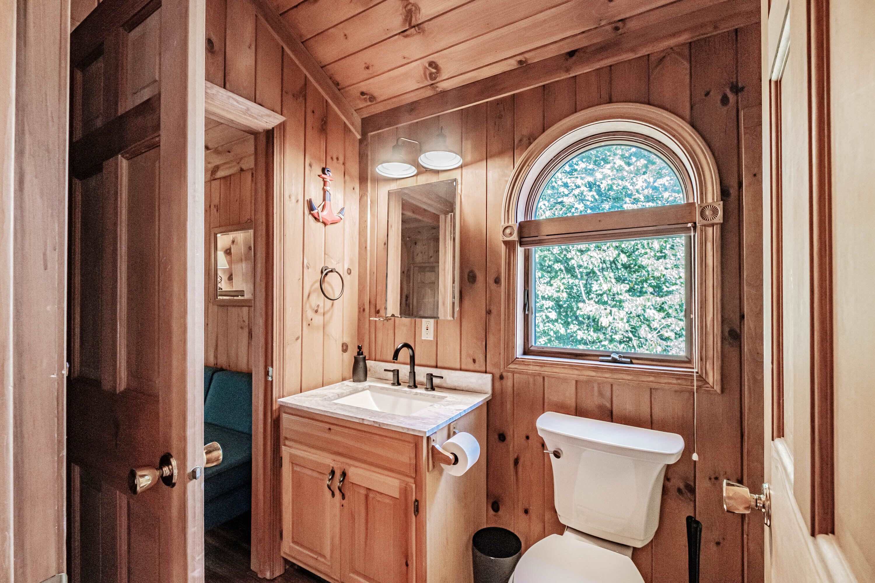 A wooden cabin bathroom with a sink, toilet, and a window with a view of trees.