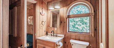 A wooden cabin bathroom with a sink, toilet, and a window with a view of trees.