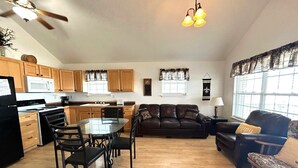 A spacious living area with a dining table, chairs, a sofa, and a coffee table. There is a kitchen area with wooden cabinets and a microwave. - La Bon Vie - Coastal Realty Group (Grand Isle)