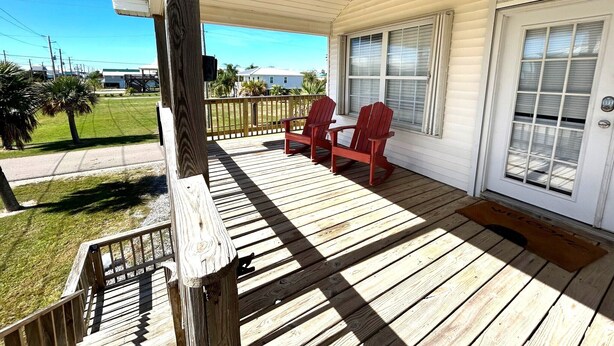 A wooden porch with two rocking chairs, a white door with a window, and a welcome mat. - La Bon Vie - Coastal Realty Group (Grand Isle)