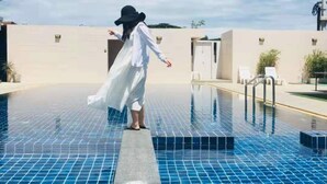 A person in a white dress and hat standing at the edge of a blue-tiled pool with a clear sky in the background. - Goodtimes Pool Villa 2 (Walk TO Beach) (Hua Hin)