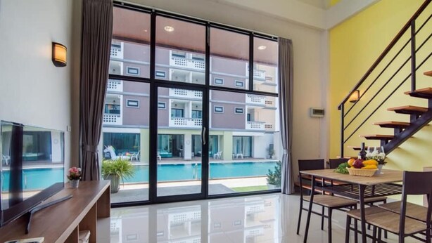 A modern living room with a large window, a pool view, a dining area, and a staircase. - Goodtimes Pool Villa 2 (Walk TO Beach) (Hua Hin)