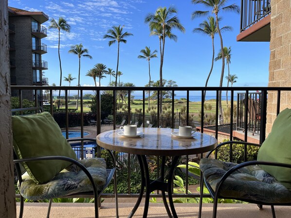 A balcony with a table and chairs, overlooking a pool and a golf course with palm trees.