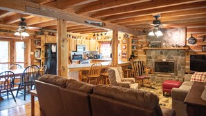 A cozy cabin interior with a wooden dining area, a living room with a fireplace, and a kitchen with stone accents. -  Rustic Log Lodge Overlooking Water and Mountain Views (Stanley)