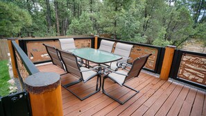 Une terrasse en bois avec une table à plateau en verre et quatre chaises.