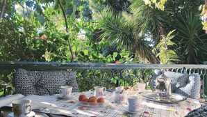 An outdoor dining area with a table set for tea, surrounded by lush greenery. - Elegant Vouliagmeni apartment in a Unique Spot. (Vouliagmeni)