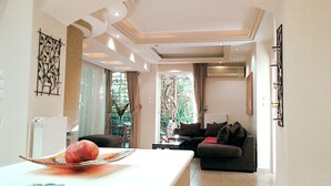 A modern living room with a dining area, featuring a large window, a sofa, a coffee table, and a decorative bowl on the table. - Elegant Vouliagmeni apartment in a Unique Spot. (Vouliagmeni)