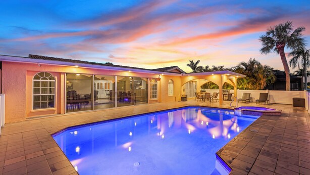 A swimming pool with a tiled deck, a covered patio area with outdoor furniture, and a sunset sky. - Water Front Home with Heated Pool & Hot Tub, 2 Master Suites & a Floating Dock (New Port Richey)