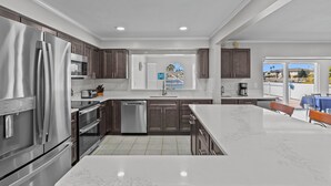 A modern kitchen with stainless steel appliances, a large island, and a view of a residential area. - Water Front Home with Heated Pool & Hot Tub, 2 Master Suites & a Floating Dock (New Port Richey)