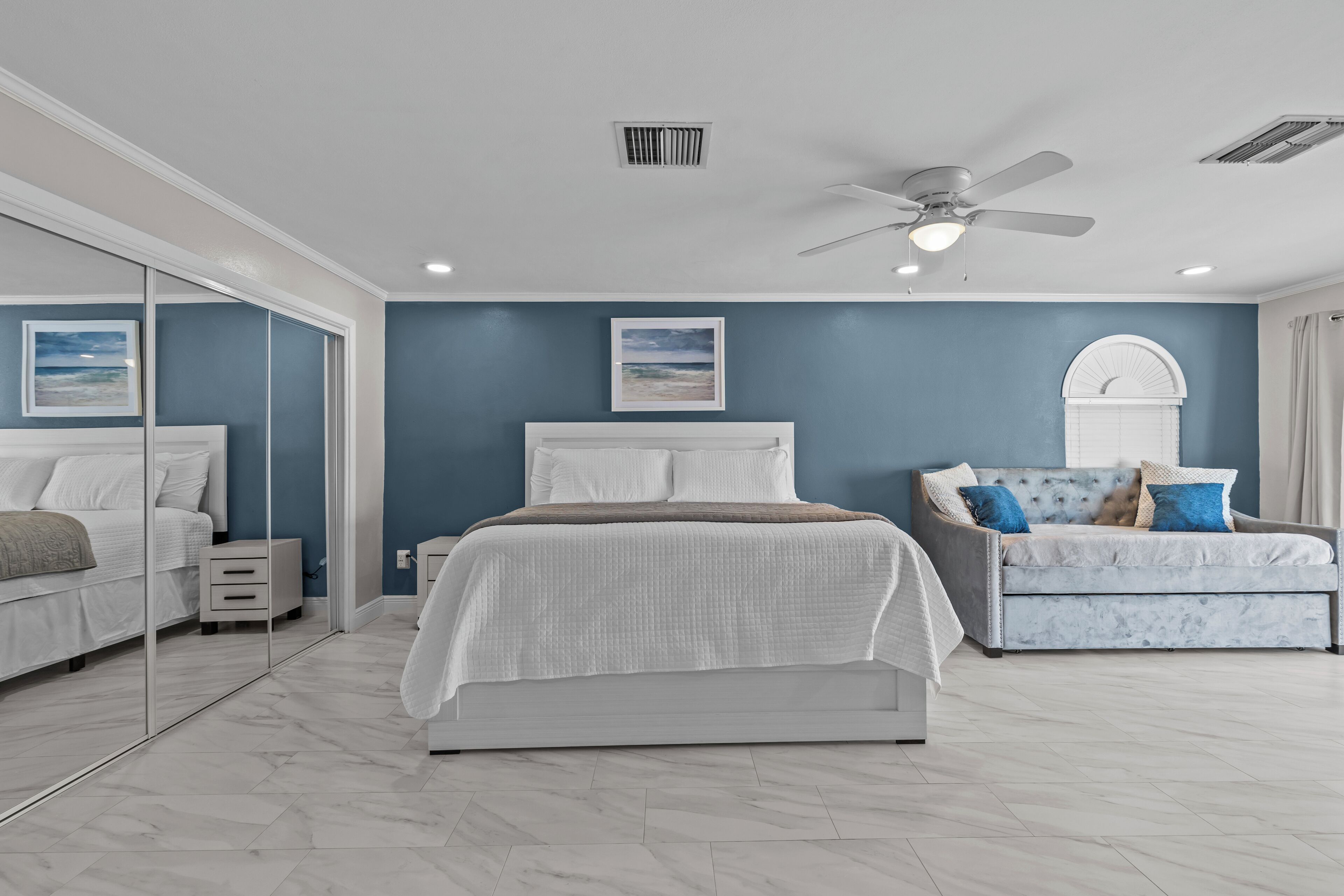 A bedroom with a bed, a nightstand, a sofa, and a ceiling fan.