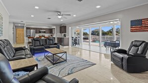 A spacious living area with a kitchen, a pool view, and a flag on the wall. - Water Front Home with Heated Pool & Hot Tub, 2 Master Suites & a Floating Dock (New Port Richey)
