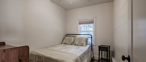A bedroom with a bed, a ceiling fan, a window, and a small table.