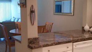 Una cocina con armarios blancos, encimera de mármol y un comedor con mesa y sillas.