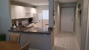 Una cocina moderna con armarios blancos, encimera de granito y comedor con mesa y sillas de madera.
