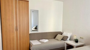 A hotel room with a wooden wardrobe, a sofa bed, a small bedside table with a lamp, and a mirror on the wall. - Villa Mihaela - Beachfront apartment "Ika" with sea view and pool (Cesarica)
