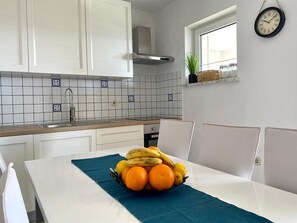 A kitchen with white cabinets, a stainless steel range hood, a tiled backsplash, a window with a plant, and a wall clock. - Villa Mihaela - Beachfront apartment "Ika" with sea view and pool (Cesarica)