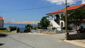 A coastal residential area with a house featuring a red-tiled roof, stone walls, and a white fence. - Villa Mihaela - Beachfront apartment "Ika" with sea view and pool (Cesarica)