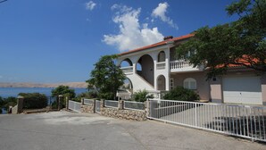 A coastal house with a stone wall, white fence, and a garage. - Villa Mihaela - Beachfront apartment "Ika" with sea view and pool (Cesarica)