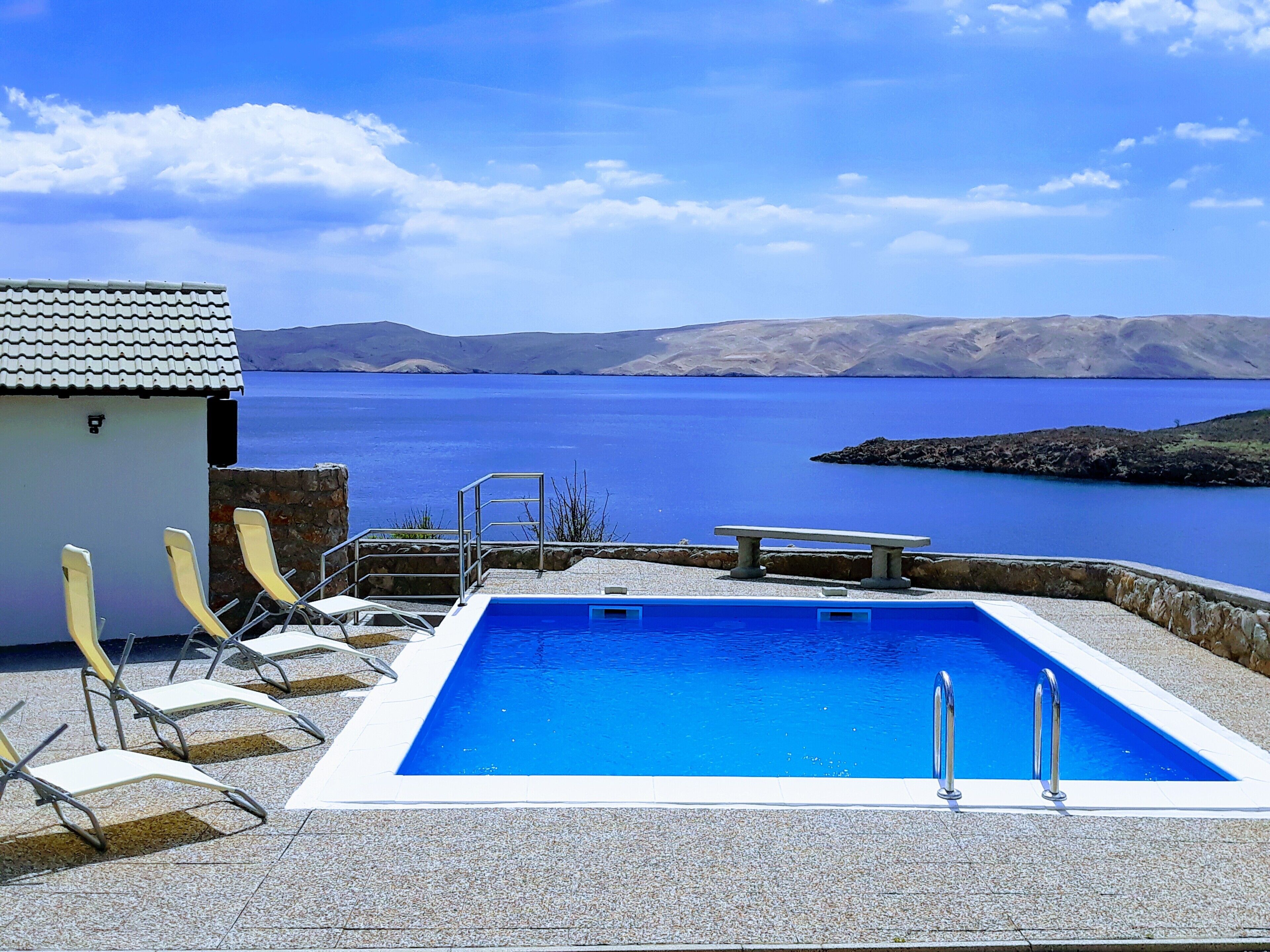 Une piscine offrant une vue sur une vaste étendue d’eau et sur des collines lointaines.