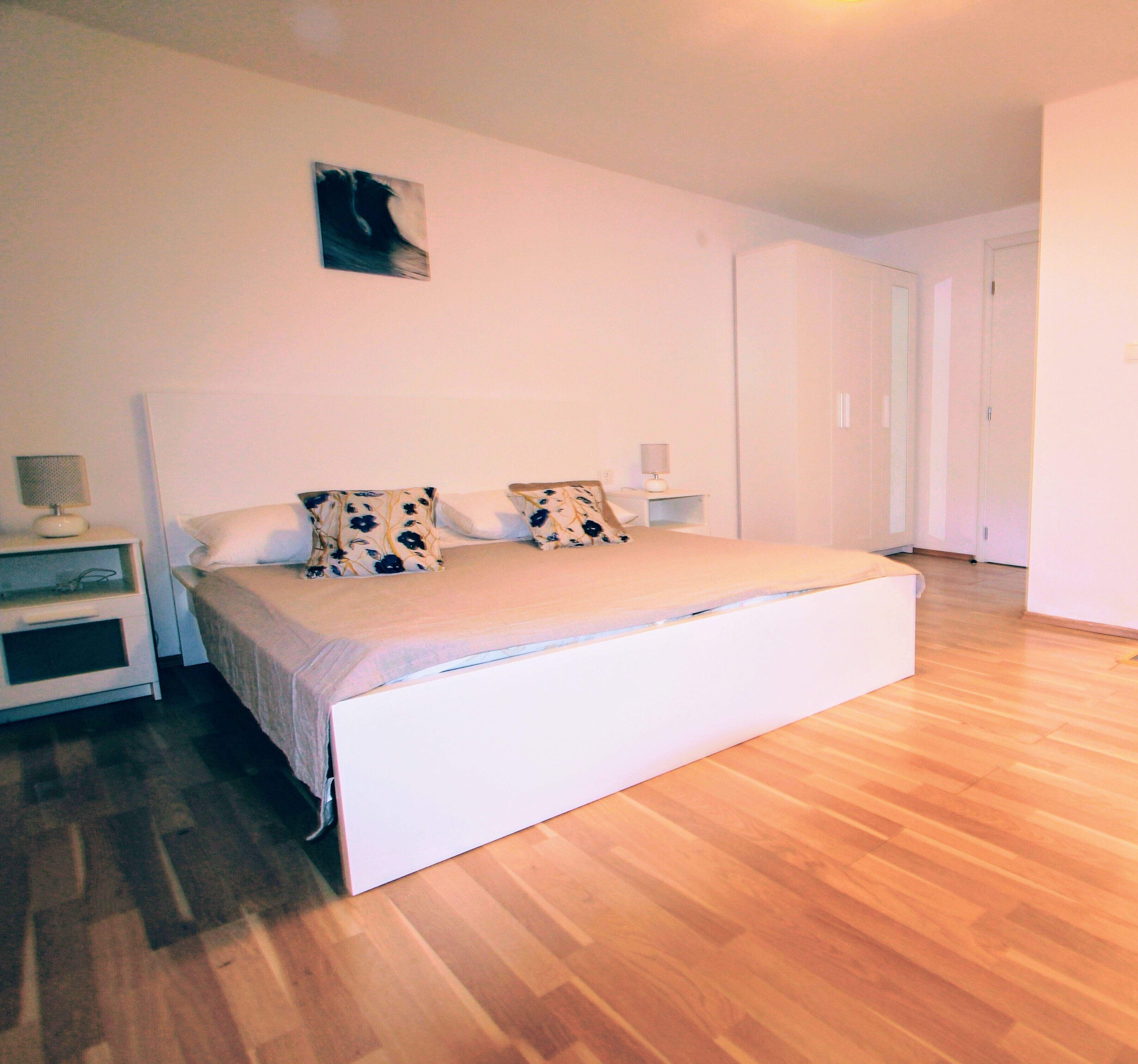 Une chambre à coucher comprenant un lit, deux tables de chevet, une petite table et une œuvre d’art accrochée au mur.