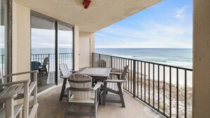Ein Balkon mit Tisch und Stühlen, der Blick auf einen Strand mit dem Meer und einem klaren Himmel bietet.